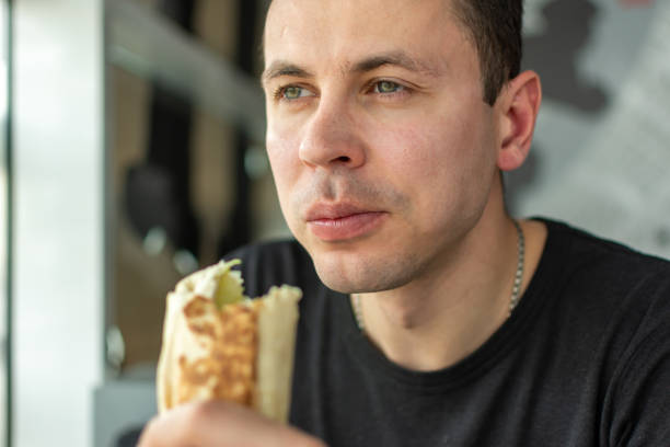 istock A man in a black tshirt satisfying his food craving by devouring a burrito 2149550038