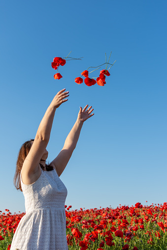 A woman in a white dress delights people in nature by throwing red flowers into the air, her joyful gesture reminiscent of petals dancing in the sky