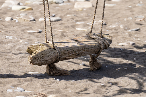 Oceanside swing made from driftwood sea logs. Vintage swing standing in the sand on the seashore.