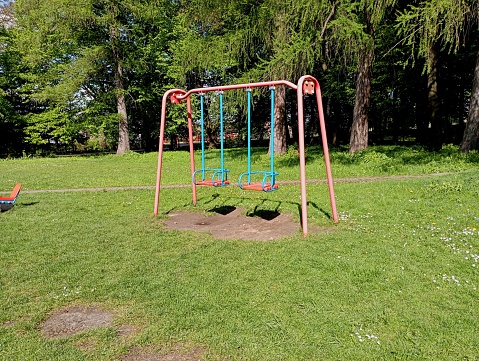 Empty swings on the playground in the park in spring. Children's attractions on the background of a green grass lawn. Entertainment for children and childhood themes.