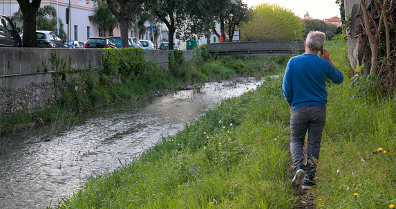Mature man walks along river and talks on phone in springtime