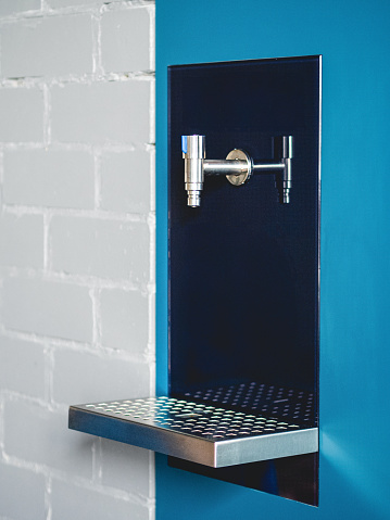 Wall-mounted drinking water dispenser with one faucet on blue and white wall