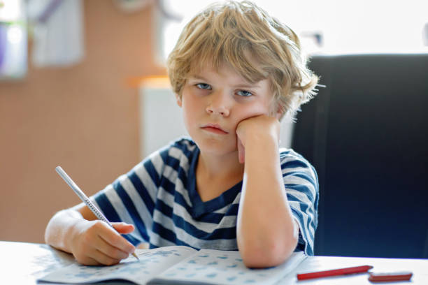 istock Portrait of tired upset boy doing homework in kitchen at home. Elementary school studing writing and learning. Sad and angry child. 2149556729
