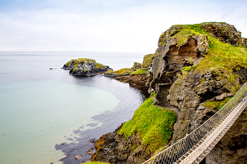 View from Carrick-a-Rede Rope Bridge, famous rope bridge near Ballintoy in County Antrim, Northern Ireland on Irish coastline. Tourist attraction, bridge to small island on cloudy day