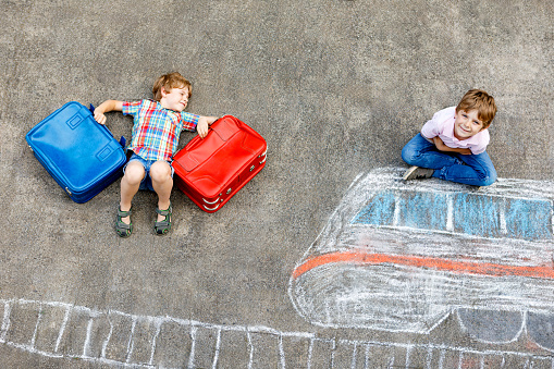 Two little kids boys having fun with train picture drawing with colorful chalks on asphalt. Children having fun with chalk and crayon painting. going on vacations and travel. Friends with suitcases.