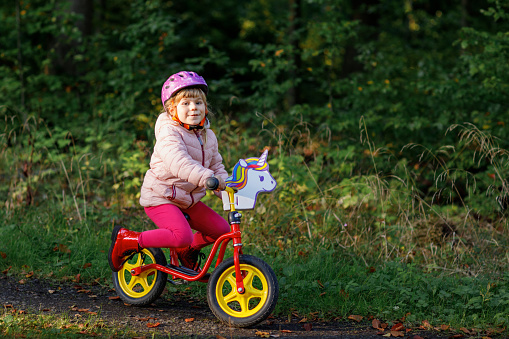 Child riding balance bike. Kids on bicycle in sunny forest. Little girl enjoying to ride glider bike on warm day. Preschooler learning to balance on run bicycle in safe helmet. Sport activity.