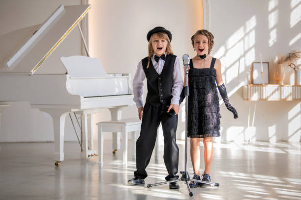 Two young children in formal wear sing a duet into a microphone. The scene is light-hearted and playful.