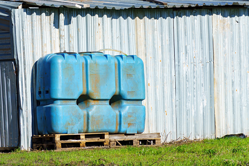 A large plastic water tank near a metal fence