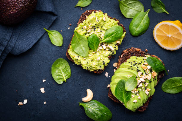 istock Avocado toasts with spinach and cashew nuts sprinkled with sesame seeds on black table background, top view 2149565068