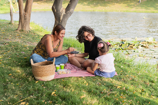 Cheerful family sharing a snack on a picnic blanket by a tranquil lakeside.