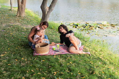 A family engages in laughter and play while lounging on a picnic blanket by a scenic lake.