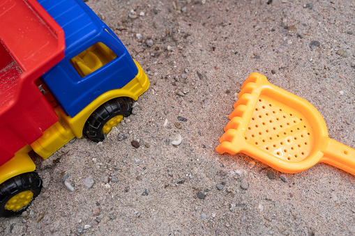 Colorful toy truck and a rake for children in the sandbox
