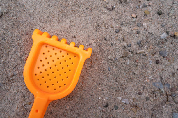 Orange colored toy rake for children in the sand