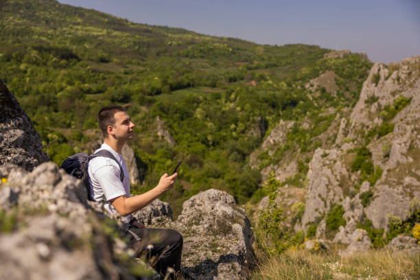 istock Young handsome hiker using mobile phone while resting on the top of a mountain 2149571728