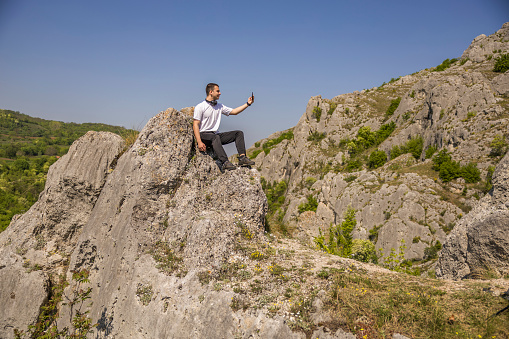 Young men is taking a selfie while sitting on the rock of the mountain.