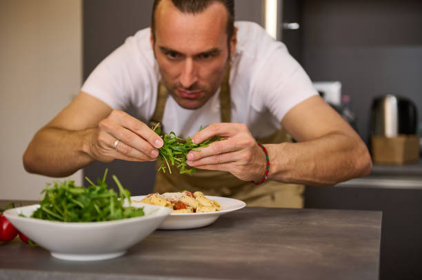 istock A man preparing dinner in home kitchen. Selective focus on hands holding greens for seasoning food. Male chef adding fresh green arugula leaves to Italian pasta with tomato sauce, garnishing the dish 2149575991