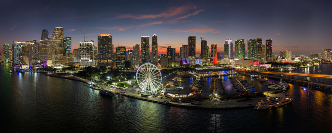 High illuminated skyscrapers of Brickell, city's financial center. Skyviews Miami Observation Wheel at Bayside Marketplace with reflections in Biscayne Bay water and US urban landscape at night.