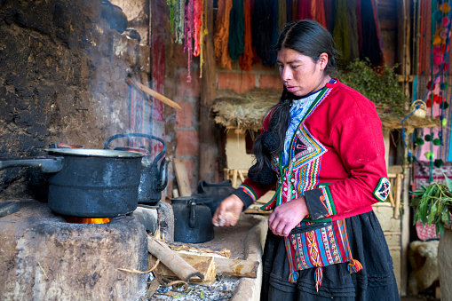 Indigenous woman weaver from the Peruvian town of Chinchero adding wood to the fire to heat the pots to create the colors to color the fabrics