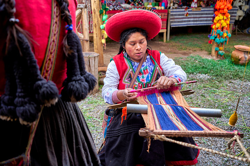 Peruvian indigenous woman from the town of Chinchero weaving cloth made with alpaca animal hair