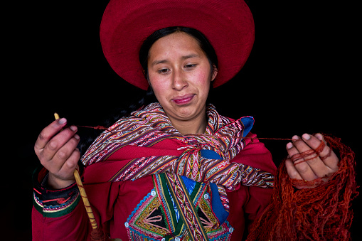 Close-up portrait with black background of a woman weaver from the Peruvian village of Chinchero with skeins of colored threads made with alpaca animal hair