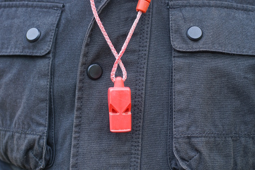 one red plastic whistle on a cord hanging from black clothes on a man on the street