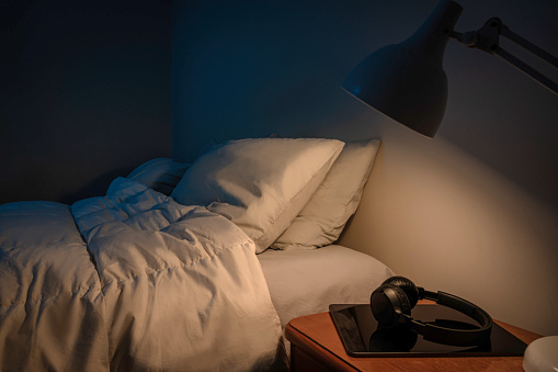 A bedroom illuminated by a night lamp and an empty bed.
