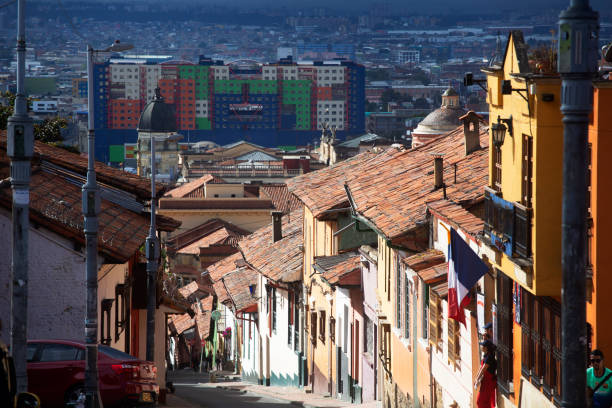Looking down a hilly street with colourful houses in an area of Bogota call La Candelaria - which is very popular with backpackers and travellers due to it's many hostels and restaurants. In the distance is a large apartment building.