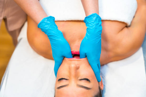 Jaw massage for bruxism and temporomandibular joint dysfunction Patient lying on clinic receiving a jaw massage for bruxism and temporomandibular joint dysfunction pain points stock pictures, royalty-free photos & images