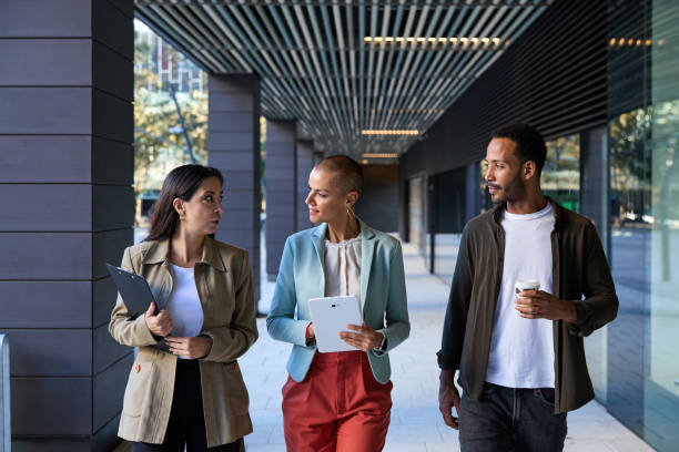istock Confident multiethnic colleagues in jackets having business conversation while walking on corridor of modern office building and looking at one another 2149583849