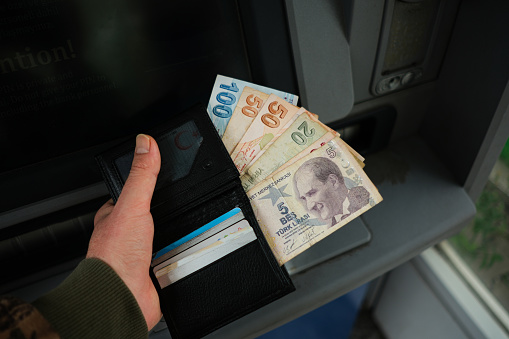 Taking out Turkish lira from a wallet in front of a cash machine