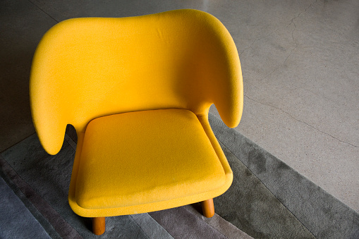 Wide yellow upholstered armchair with fabric upholstery on wooden legs, retro style.