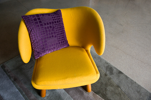 Wide yellow upholstered armchair with fabric upholstery on wooden legs, retro style.