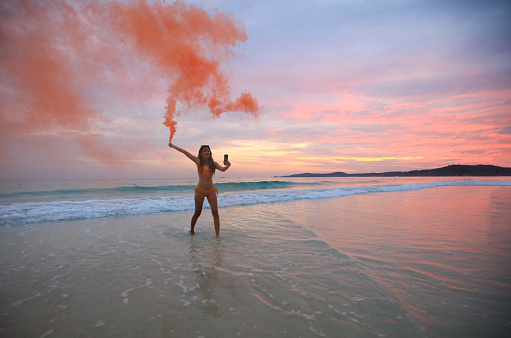 A funny sexy woman with a swimming suit handles color smoke dances relaxes on a tropical beach, Summer Vacation