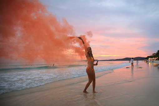 Happy charming  woman holding colored smoke bombs and having fun on the beach