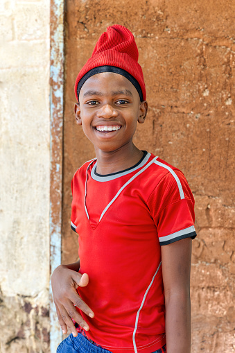 smiling african villager child with a beanie playing outdoors in front of the house in a village,