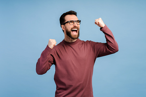 Attractive overjoyed bearded man, winner win money happy, gesturing, posing isolated on blue background. Victory concept