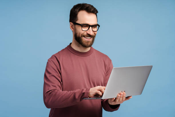 istock Young man, bearded freelancer, hipster wearing eyeglasses holding laptop, typing on keyboard 2149588975