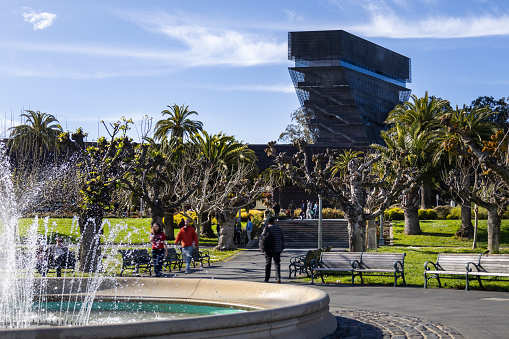 San Francisco, CA, USA. March 30, 2024 : A serene scene in front of the de Young Museum, featuring a vibrant fountain and lush tropical trees.