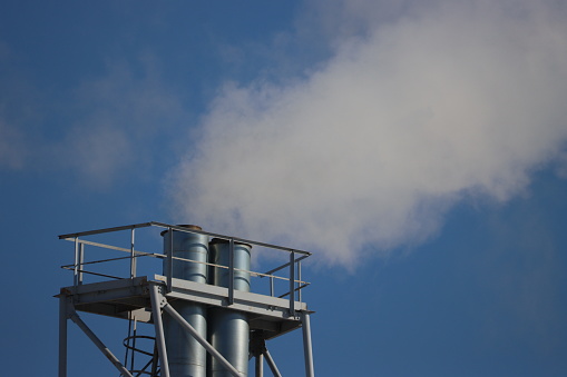 The chimney of a heating station and white smoke coming from it against the background of a blue sky.