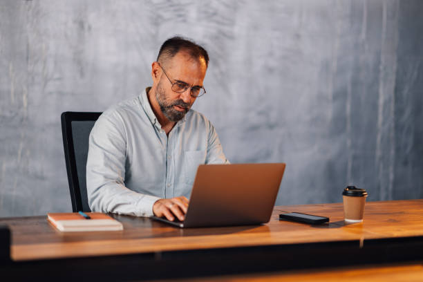 istock Mature businessman typing on a laptop at modern corporate office. 2149591493