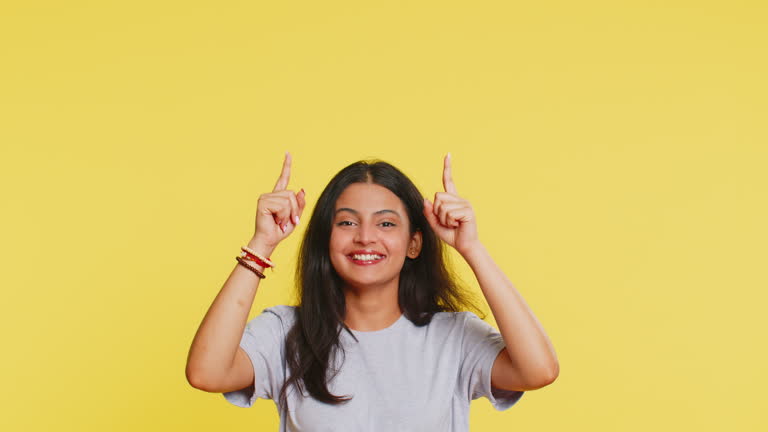 Young woman showing thumbs up and pointing overhead on blank space place for your advertisement logo