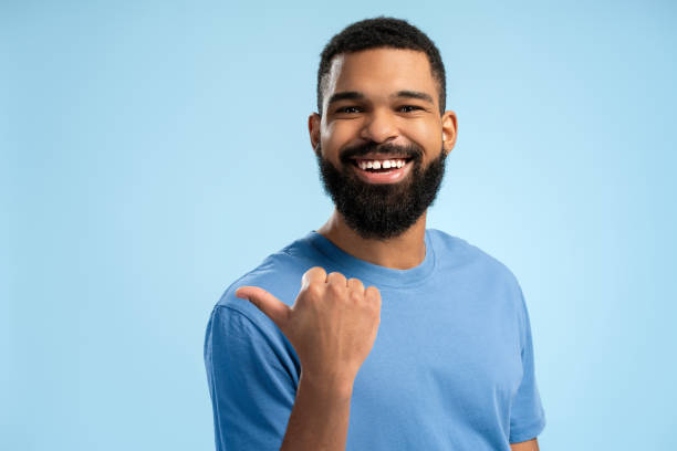 istock Smiling African American man pointing to the side with thumb up over blue background with copy space 2149593373