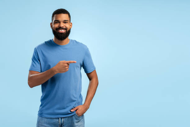 istock Smiling bearded African American young man pointing to his side in studio over blue background 2149593376