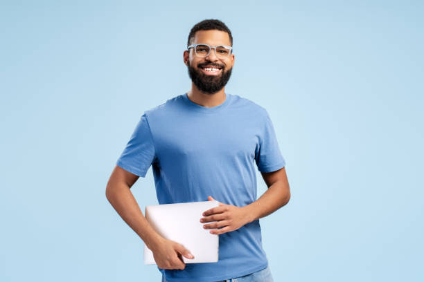 istock Happy African American in eyeglasses holding laptop while looking at camera, over blue background 2149593422