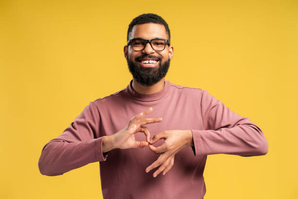 Smiling African American man in eyeglasses showing word interpreter over yellow background Happy bearded African American man posing in studio and showing word interpreter, isolated on yellow background. People lifestyle concept sign language stock pictures, royalty-free photos & images