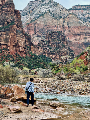 Young adult is surrounded by majestic beauty as she walks through one of the canyons at Zion National Park in Utah
