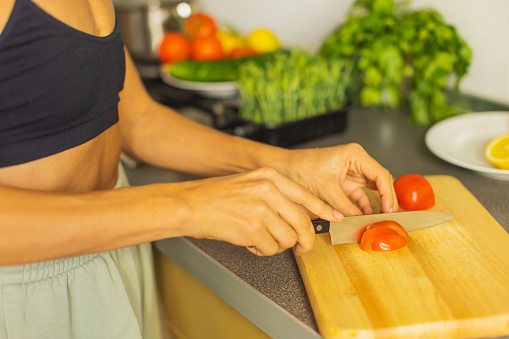 Woman cutting tomato on kitchen board.