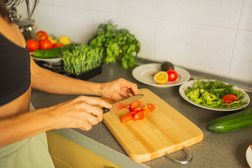 Woman cutting tomato on kitchen board.