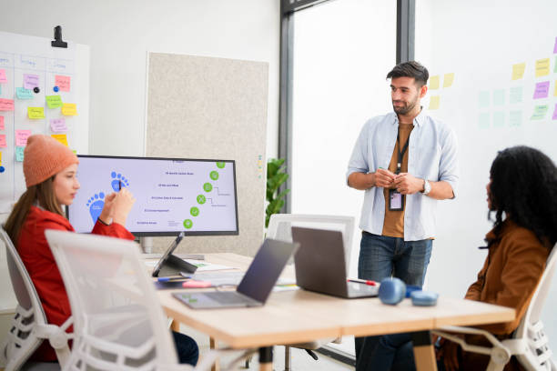 istock Confident male leader conducts a workshop, explaining ideas with sticky notes on a glass wall to colleagues. 2149597503