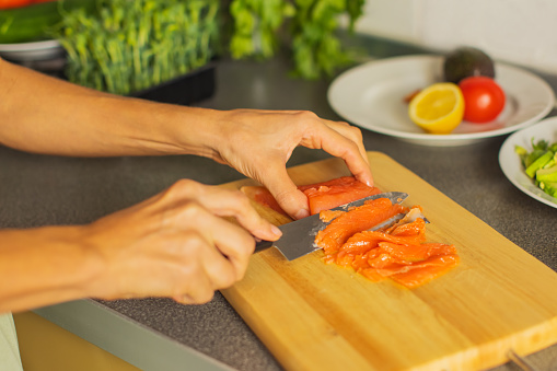 Woman cutting red fish on kitchen board.